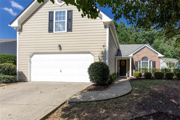 Exterior featuring brick and siding facade, a two-car garage, a front walkway, and mature landscaping