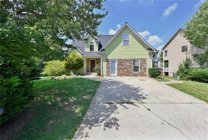 Light green siding with stone veneer accents, gabled roofline, front-facing windows, and a concrete driveway