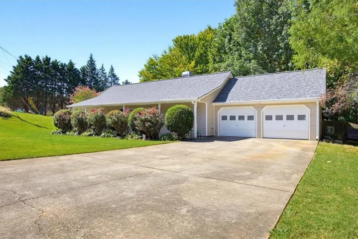 Single-story exterior with light-toned siding, a multi-car garage with white paneled doors, and a concrete driveway