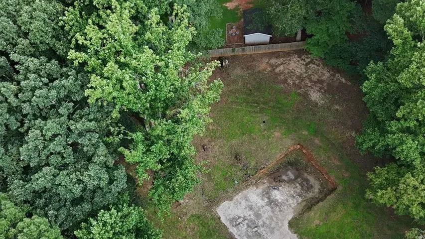 Expansive lot featuring a cleared building footprint, mature perimeter trees, and a partially excavated area