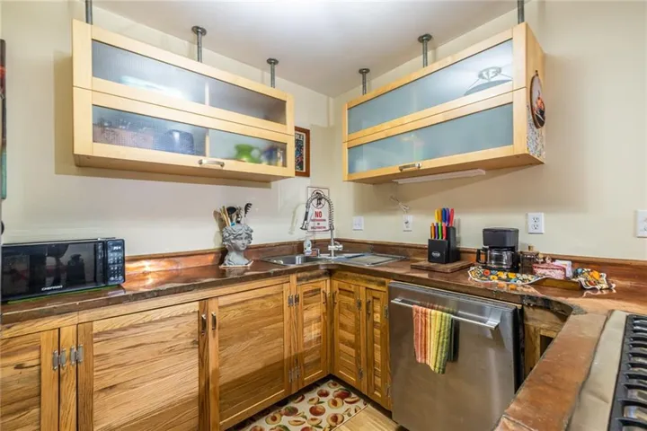 Kitchen featuring wood-finish cabinetry, stainless steel sink, integrated dishwasher, and wood-finish countertops