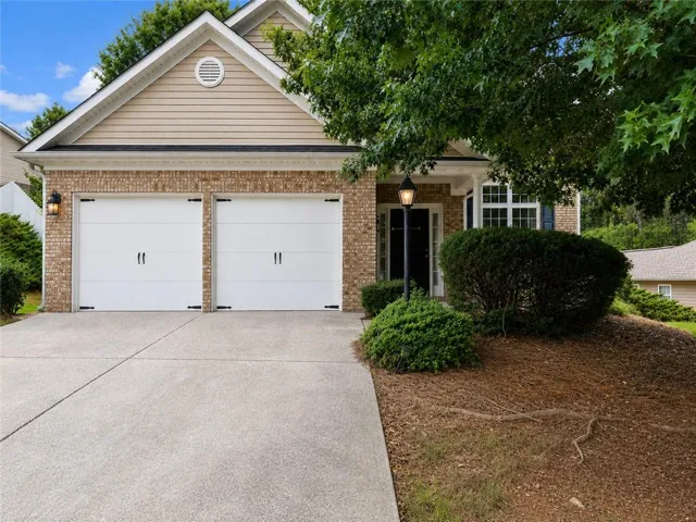 Front exterior featuring a two-car garage with white doors, brick facade, light-toned siding, a concrete driveway, and mature landscaping