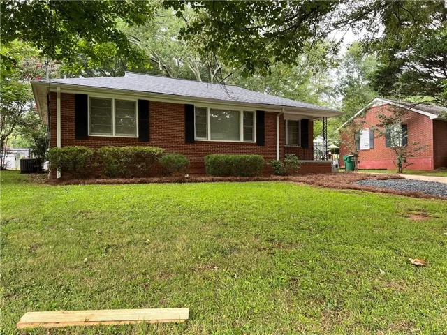 Brick ranch-style residence featuring a covered front porch, dark-colored shutters, and a well-maintained shrub line