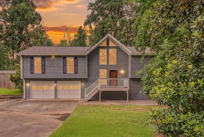 Split-level home featuring grey siding, a two-car garage, and an elevated front porch