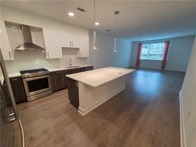 Open-concept kitchen featuring an oversized island with countertop seating, stainless steel appliances, and wood-finish flooring throughout