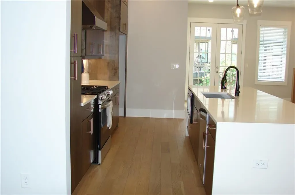 Kitchen with modern cabinets, stainless steel appliances, light wood-style floors, light stone countertops, and range hood