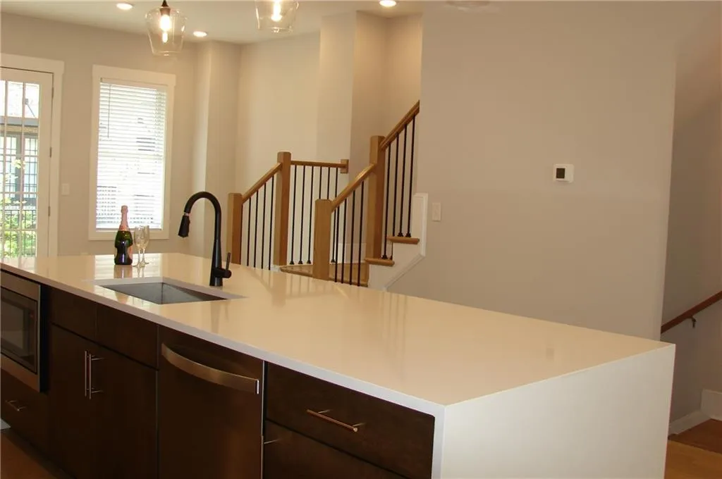 Kitchen with wood finish cabinetry, stainless steel appliances, light stone countertops, a center island with sink, and modern cabinets