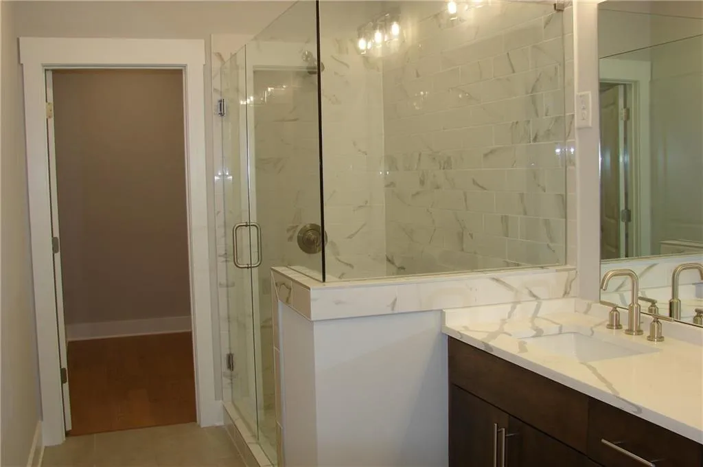 Primary bathroom with a marble finish shower, vanity, and light tile patterned flooring