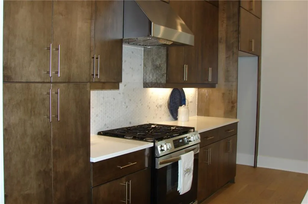 Kitchen with stainless steel gas range oven, ventilation hood, light wood finished floors, tasteful backsplash, and wood finish cabinets