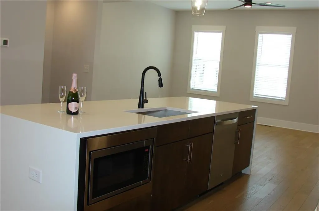 Kitchen featuring wood finish cabinetry, stainless steel appliances, light wood-style flooring, a center island with sink, and light stone counters