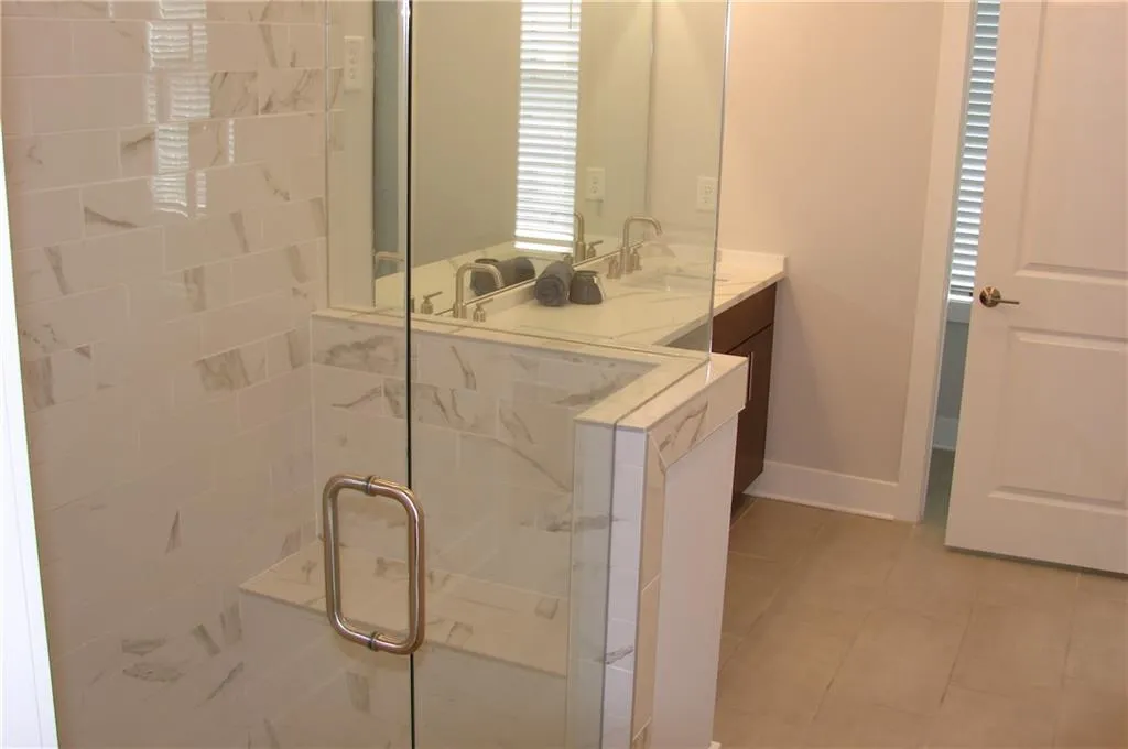 Primary bathroom featuring vanity, a marble finish large walk-in shower, and light tile patterned floors