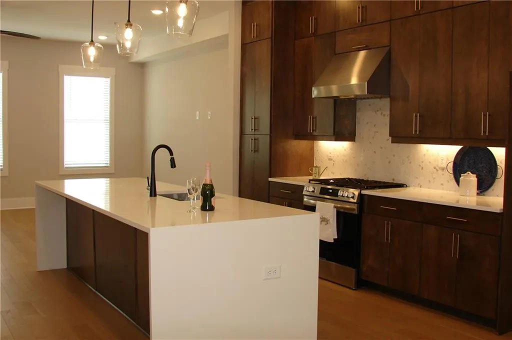 Kitchen featuring gas range, tasteful backsplash, wood finish cabinets, a kitchen island with sink, and light stone counters