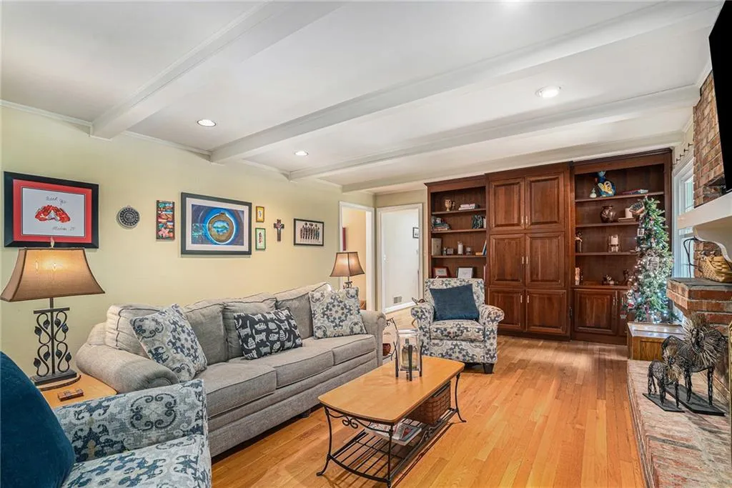 Living room featuring brick wall, crown molding, light hardwood / wood-style floors, and beam ceiling
