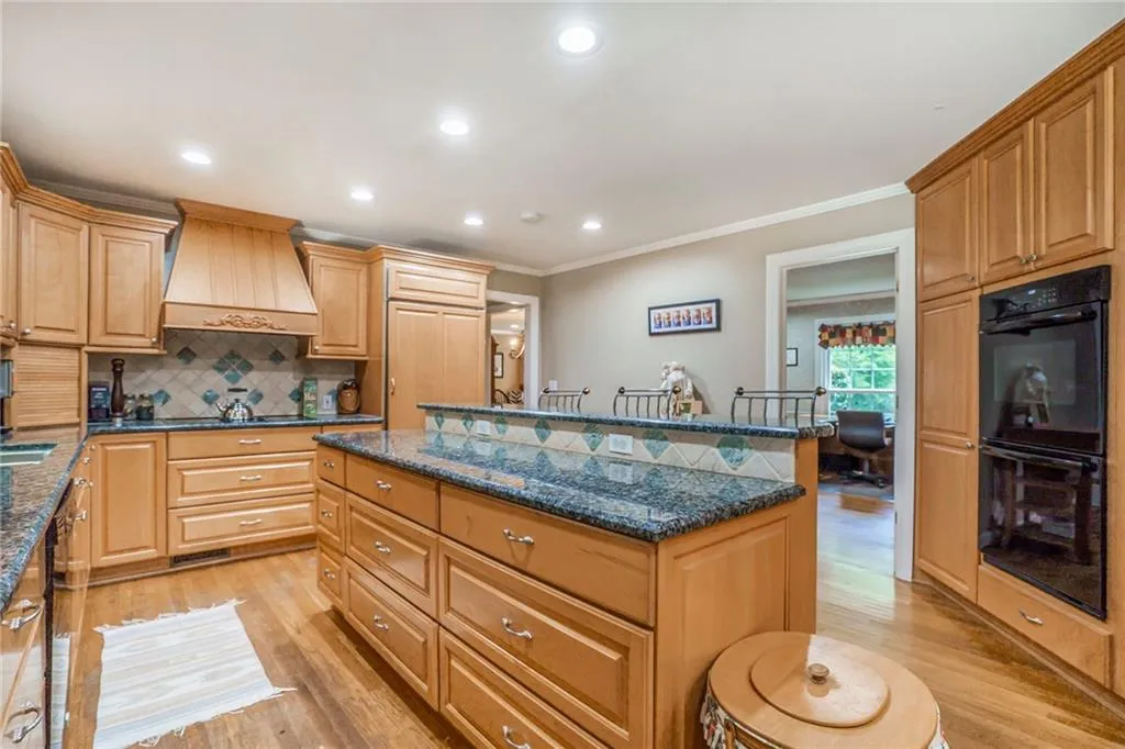 Kitchen with decorative backsplash, dark stone countertops, black appliances, and light wood-type flooring