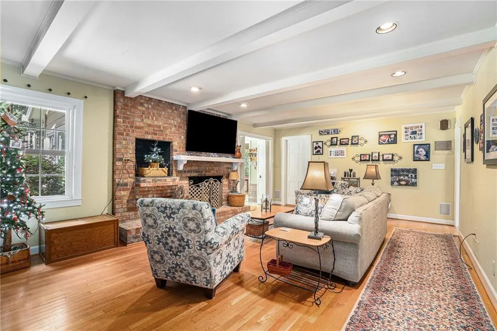 Living room with light hardwood / wood-style floors, beam ceiling, ornamental molding, and a brick fireplace
