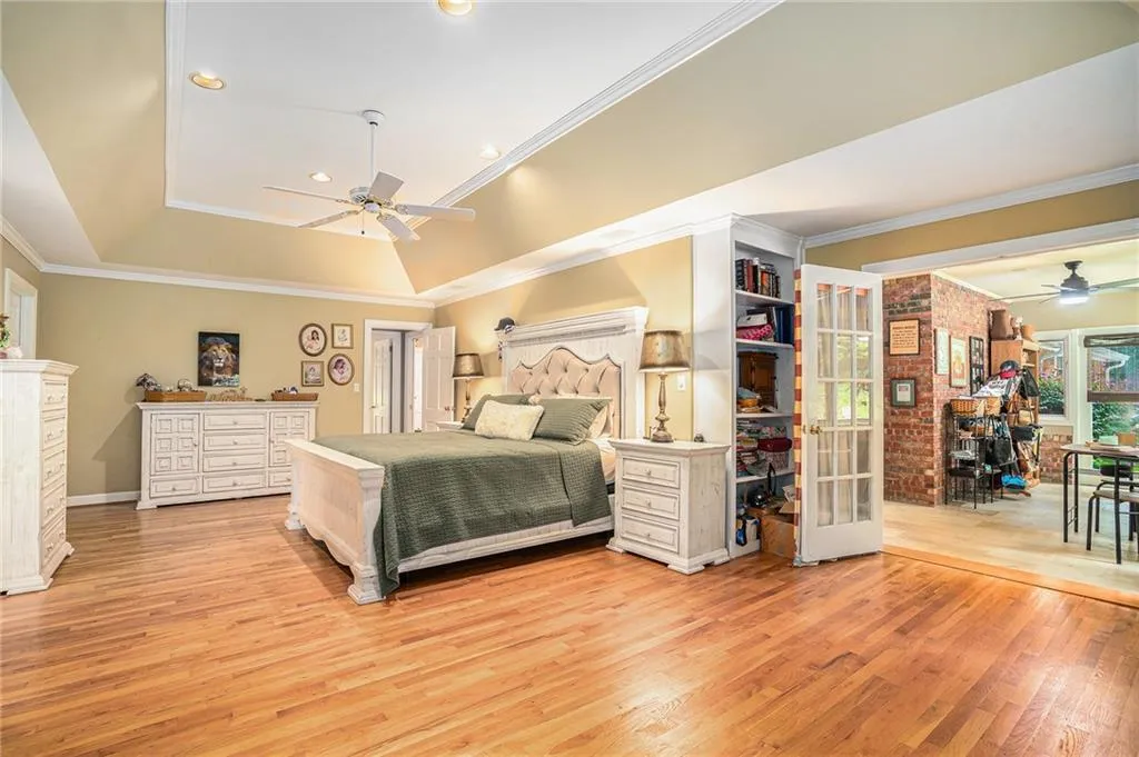 Bedroom with crown molding, ceiling fan, wood-type flooring, and a raised ceiling