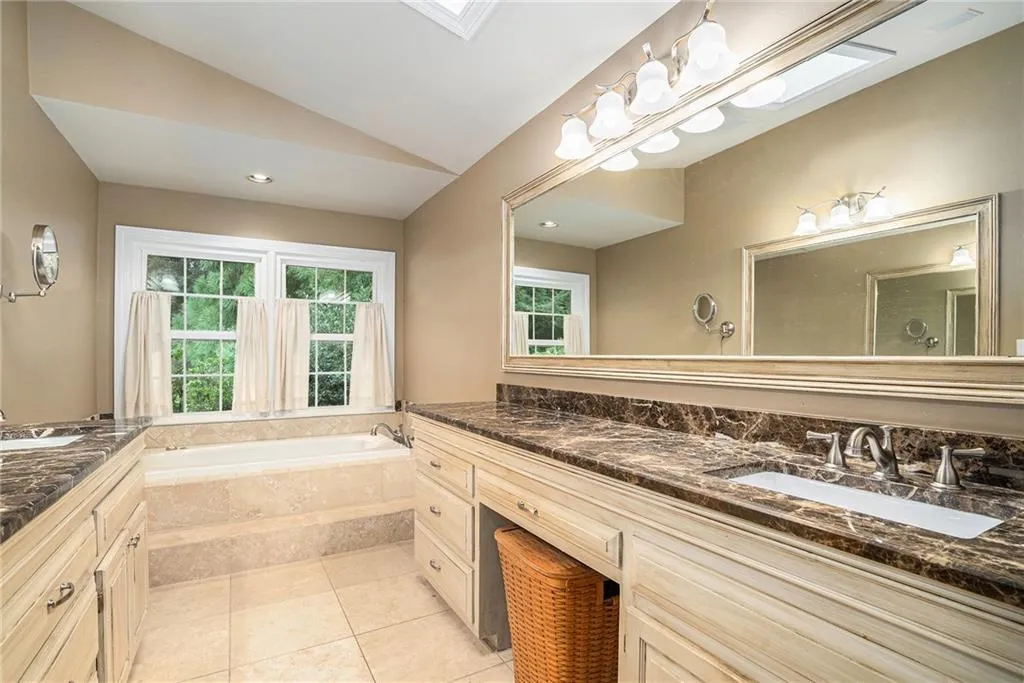 Bathroom featuring a relaxing tiled tub, vanity, lofted ceiling, and tile patterned floors