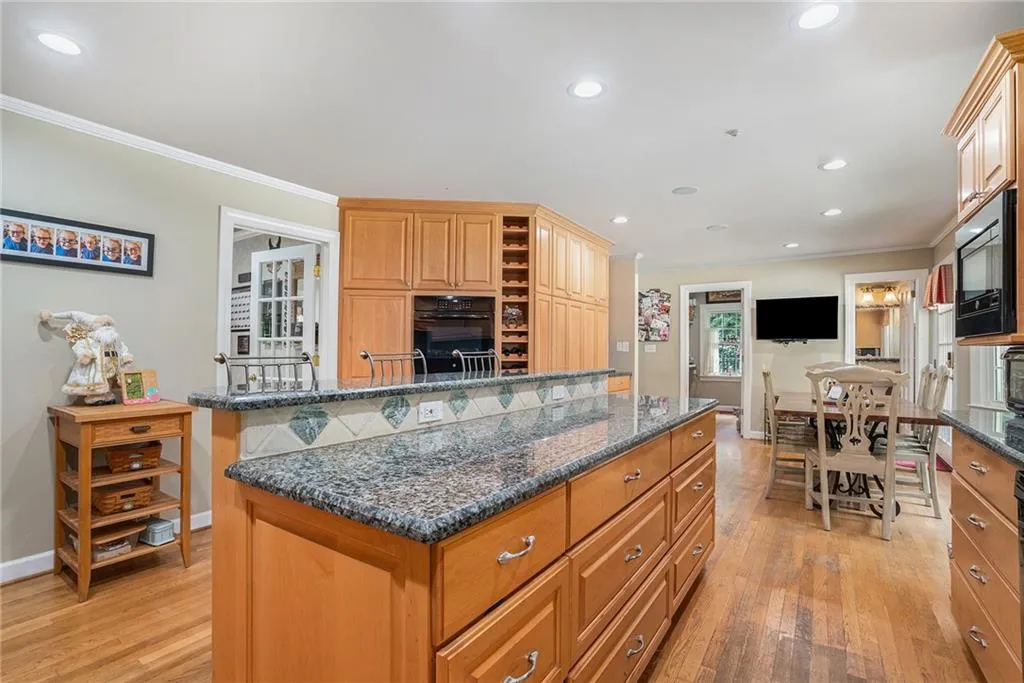 Kitchen with crown molding, dark stone countertops, stainless steel microwave, light hardwood / wood-style flooring, and black oven