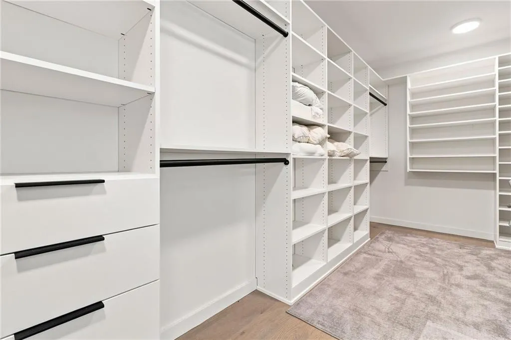 Custom closet system featuring white shelving, integrated drawers with black hardware, black hanging rods, and wood-finish flooring