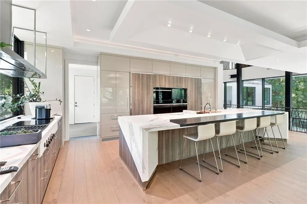 Modern kitchen featuring wood-finish flooring, a large island with an integrated sink, built-in appliances, and expansive windows