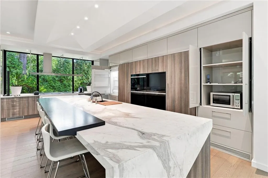 Modern kitchen featuring a large waterfall island, integrated appliances, wood-finish flooring, full-height cabinetry, and expansive windows