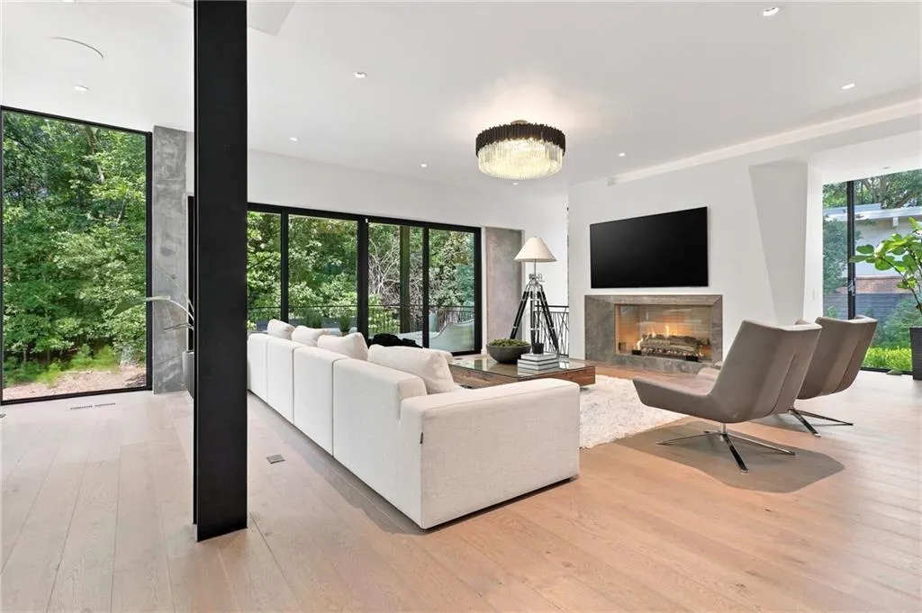 Expansive wood-finish flooring, full-height windows, a built-in fireplace with stone surround, a recessed ceiling, and a modern chandelier