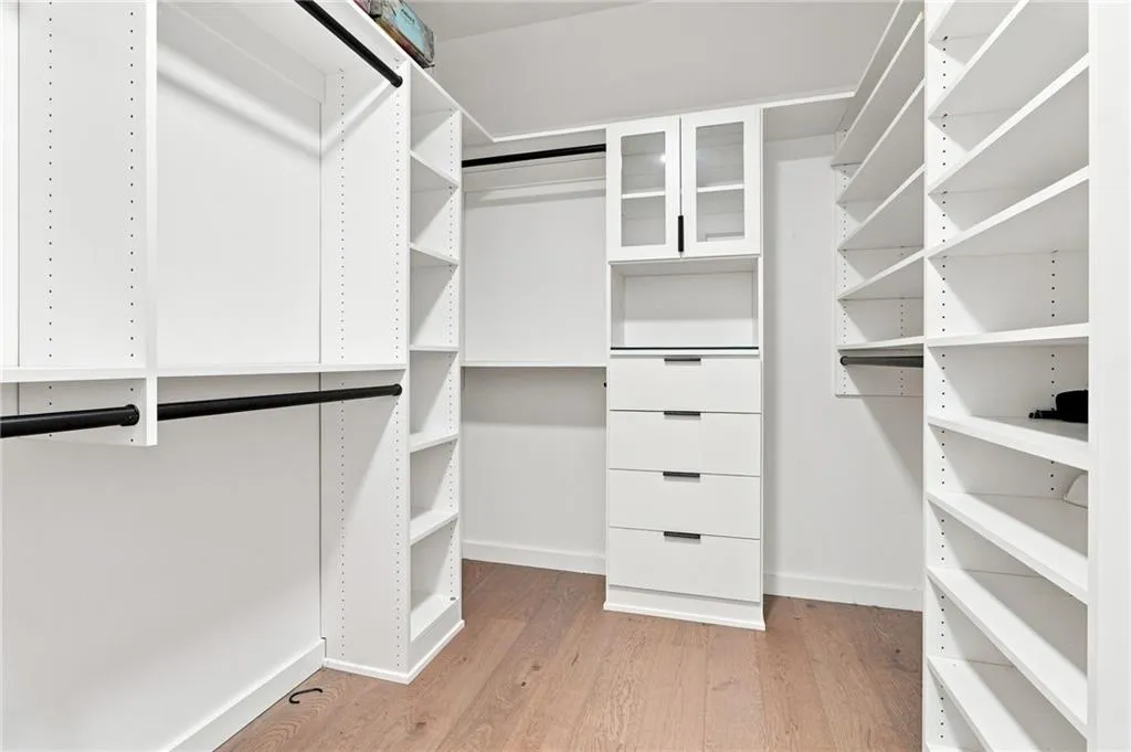 Integrated white custom closet system with adjustable shelving, multiple hanging rods, built-in drawers, and glass-front cabinets