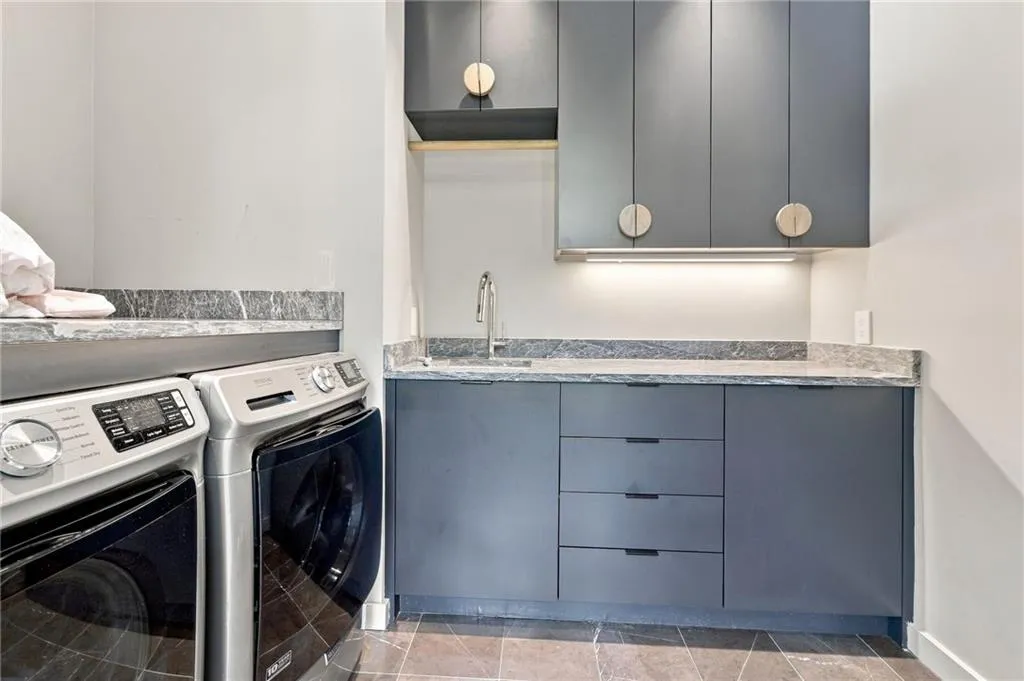 Integrated laundry area featuring stone countertops, built-in cabinetry, a utility sink, and under-cabinet lighting