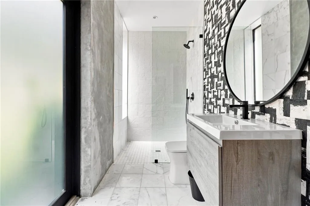 Walk-in shower with glass enclosure, single vanity with integrated sink, black-framed oval mirror, and a frosted glass window