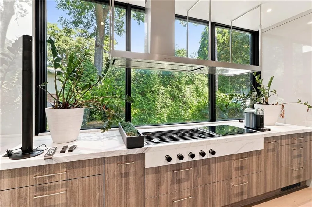 Modern kitchen with wood-finish cabinetry, light-toned countertops, and a built-in cooktop with an overhead range hood