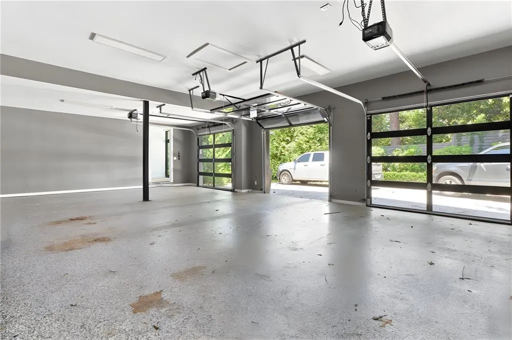 Three-bay garage with modern glass-paneled doors, exposed beam ceiling, and overhead lighting