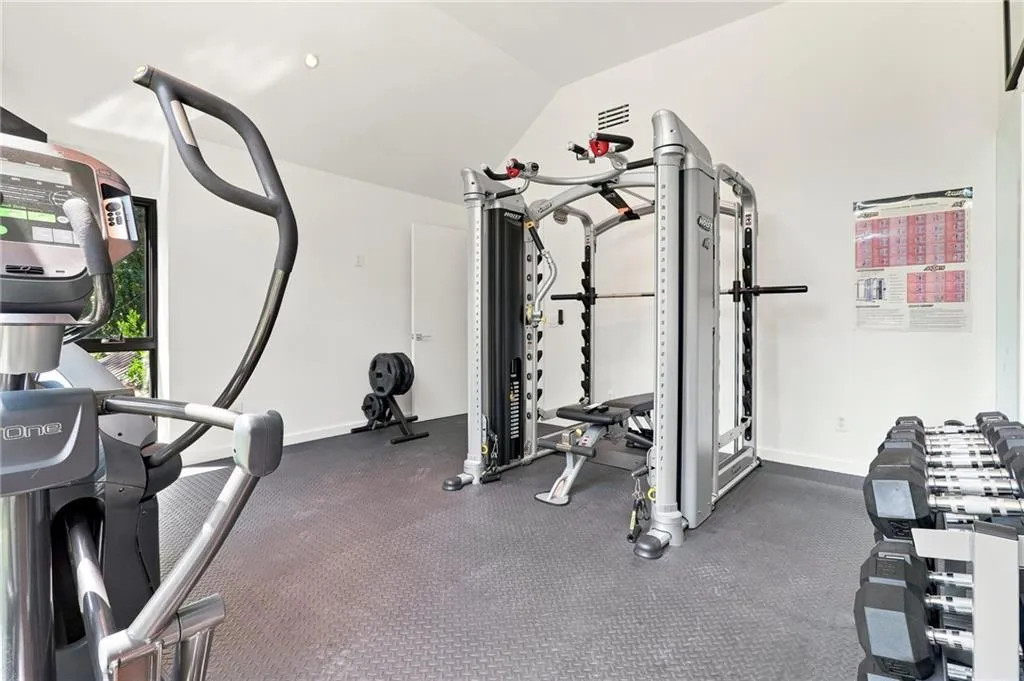 Fitness room featuring rubberized flooring, white walls, and a vaulted ceiling