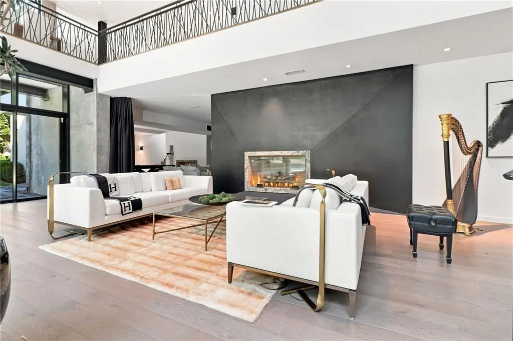 Double-height living area featuring wood-finish flooring, an angular dark-toned fireplace surround with a gas fireplace, and a second-story interior balcony with an ornate railing