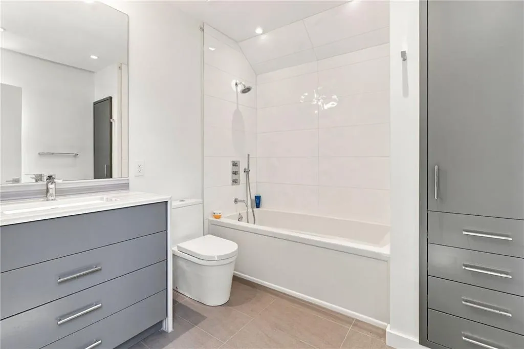 Bathroom featuring a white subway-tiled shower, white bathtub, sleek vanity with a single sink, and integrated storage cabinetry
