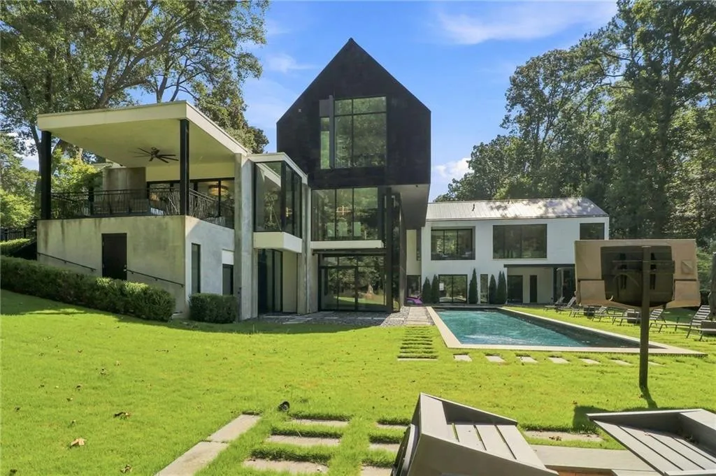 Modern architectural design featuring a rectangular swimming pool, concrete patio, expansive lawn, and a covered balcony with a ceiling fan
