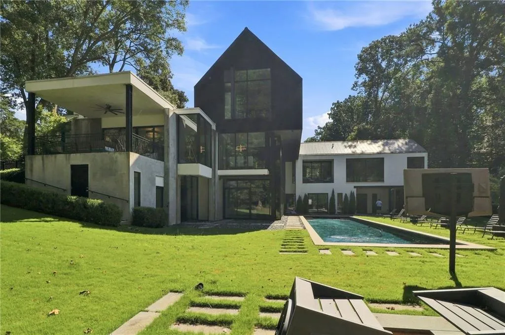 Contemporary architecture featuring a black facade, a rectangular swimming pool, expansive glass panels, a covered outdoor living area, and a flat roofline