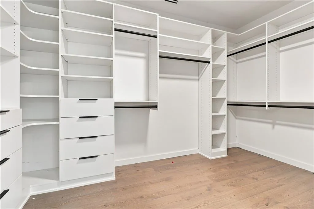 Custom closet system featuring white shelving, multiple hanging rods, built-in drawers with modern pulls, and wood-finish flooring