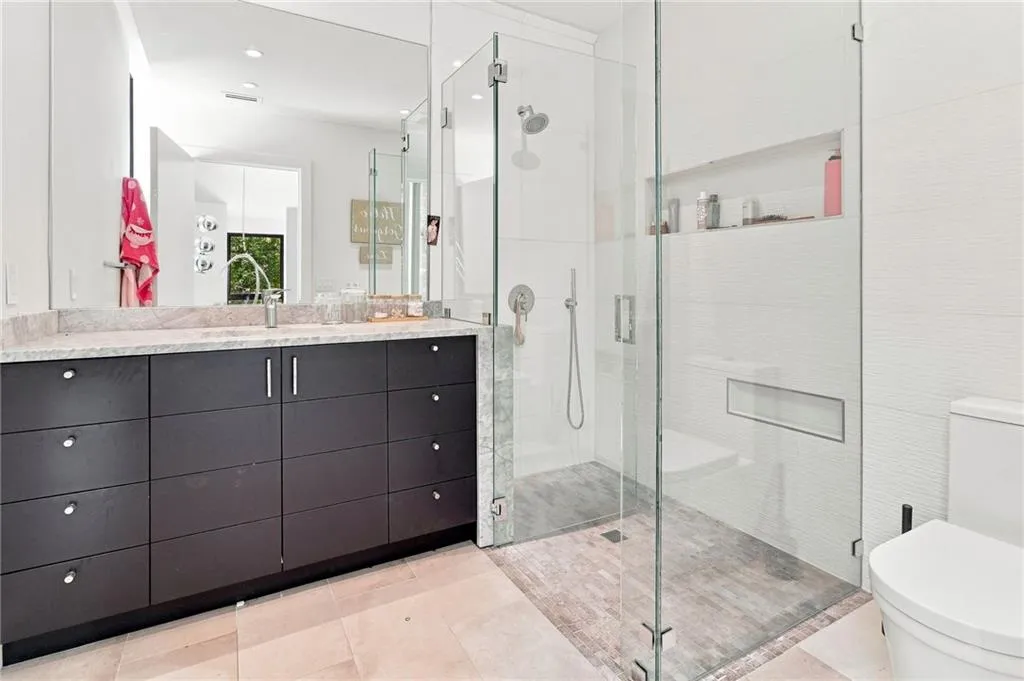 Dual-sink vanity with a light-toned countertop, dark wood-finish cabinetry, and a frameless glass-enclosed shower with an integrated niche