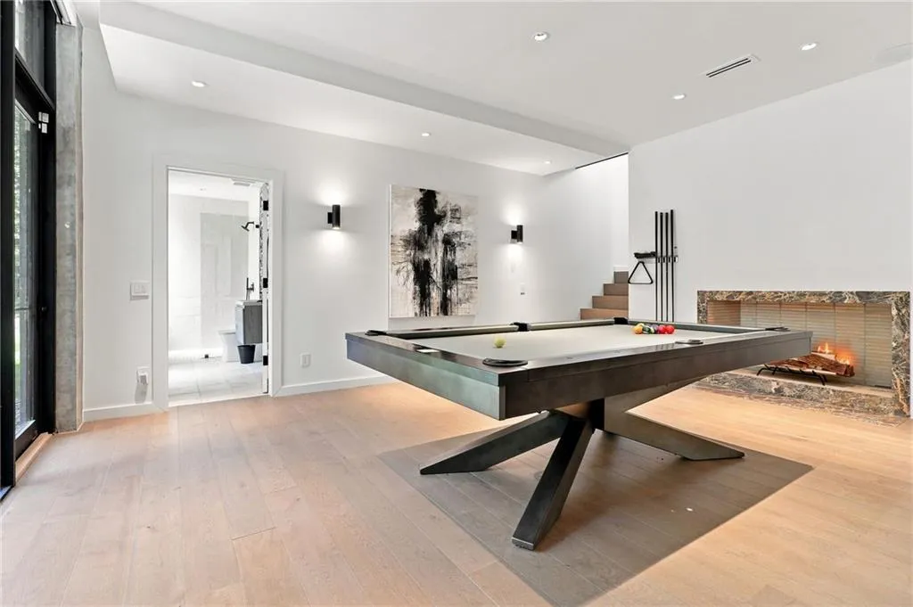 Recessed lighting, wood-finish flooring, stone-clad fireplace, built-in staircase, and a visible doorway to an adjacent bathroom