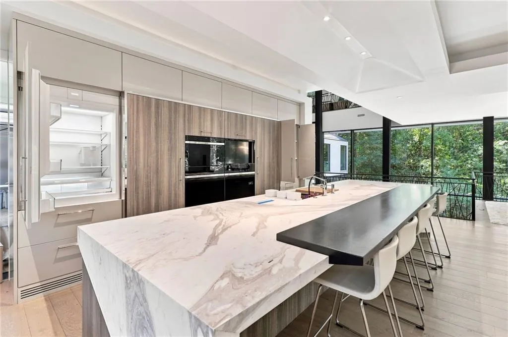 Waterfall island with integrated sink, wood-finish flooring, built-in panel-front refrigerator, built-in wall ovens, and expansive windows