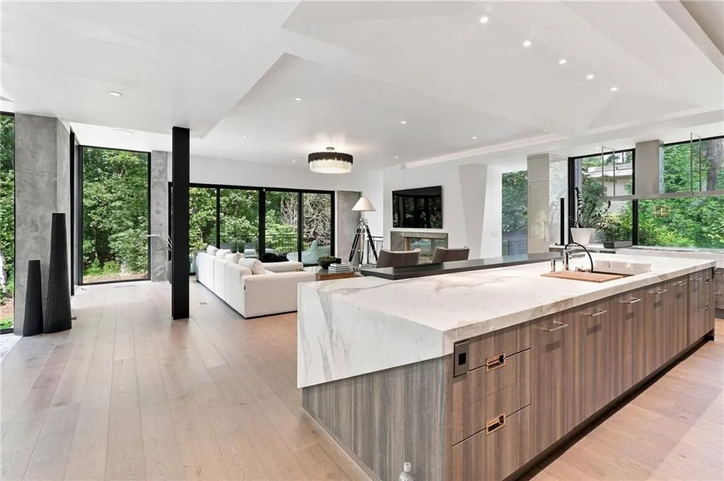 Open-concept living space featuring wood-finish flooring, a kitchen island with integrated sink, and large format windows