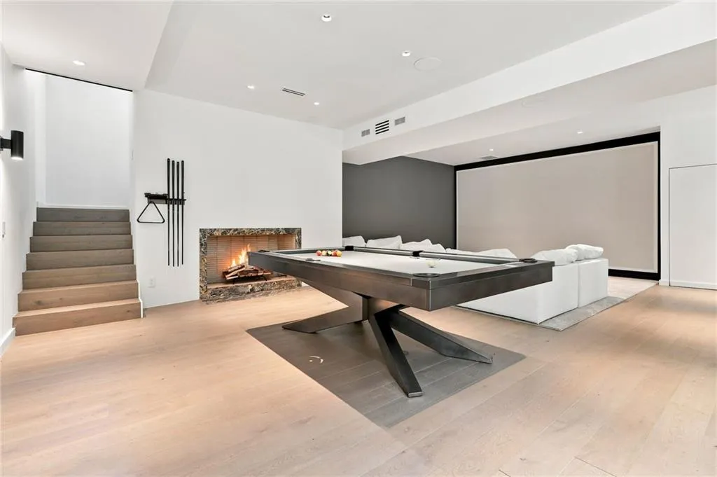 Recessed lighting, wood-finish flooring, stone-clad fireplace, built-in projection screen, and an open staircase