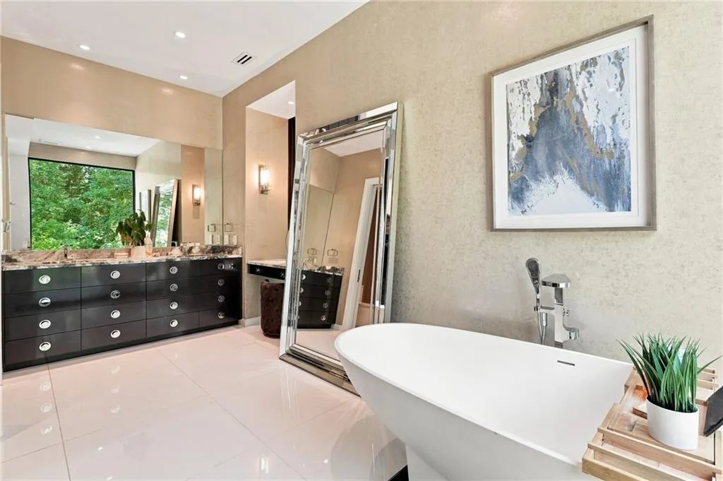 Freestanding soaking tub with chrome fixtures, dual vanity with dark wood cabinetry, large inset mirror, and recessed lighting