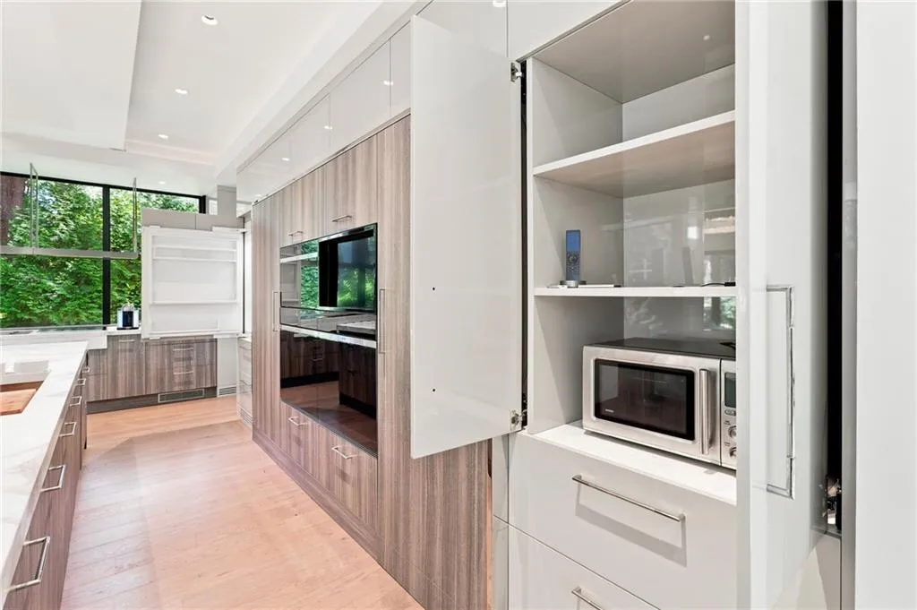 Modern kitchen featuring light wood-finish flooring, built-in wall ovens, and custom cabinetry with varied finishes