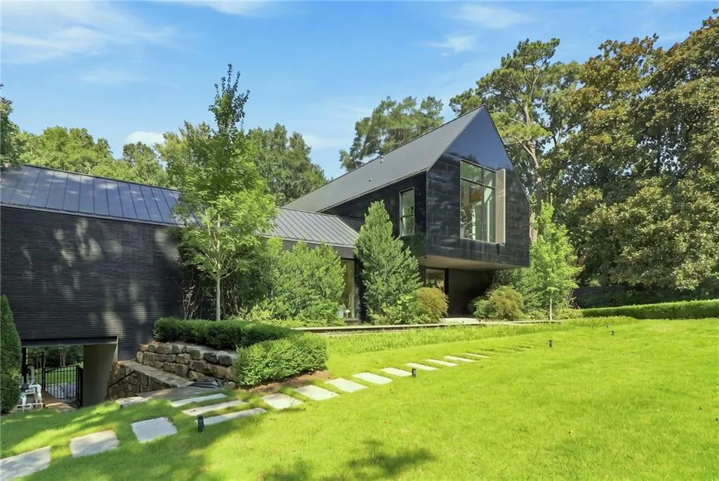 Modern architectural exterior featuring a dark facade, metal roofing, large window expanses, and an expansive lawn with stone step pathways