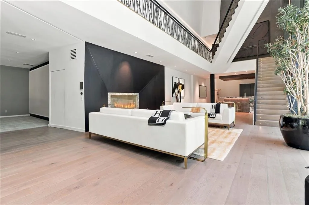 Open-concept living area featuring light wood-finish flooring, a contemporary fireplace with a dark accent wall, and a multi-level staircase with decorative metal railings