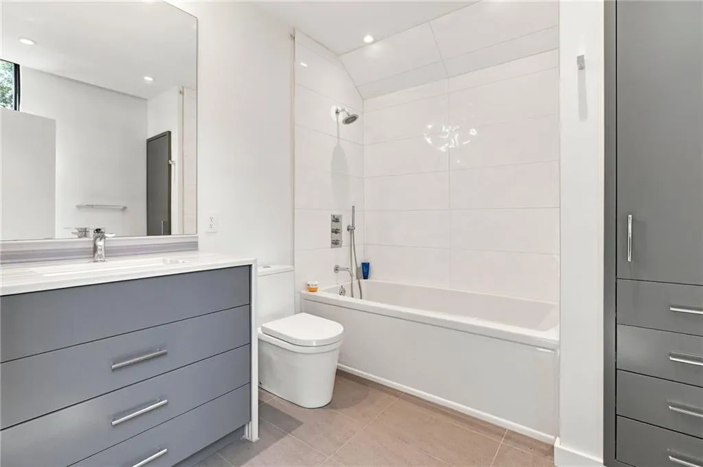 Contemporary bathroom featuring a white soaking tub with a shower fixture, a sleek vanity with a solid surface countertop, a large mirror, and integrated recessed lighting