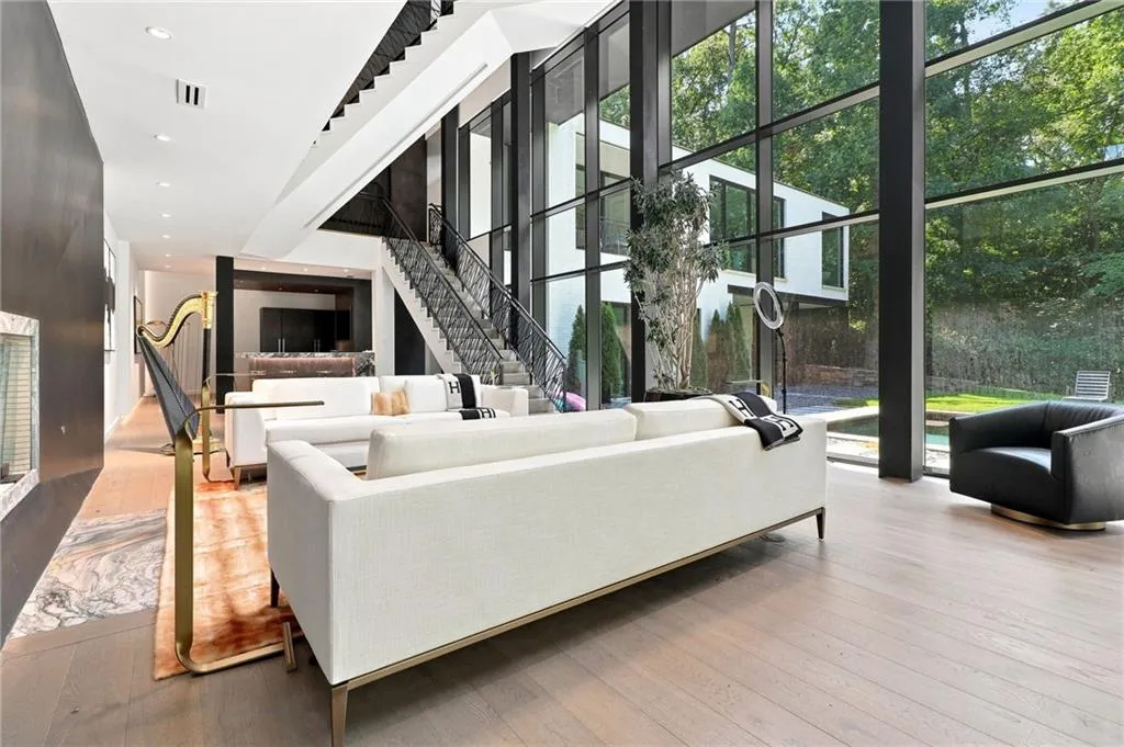 Double-height living space featuring expansive floor-to-ceiling windows, modern wood-finish flooring, and a contemporary metal staircase