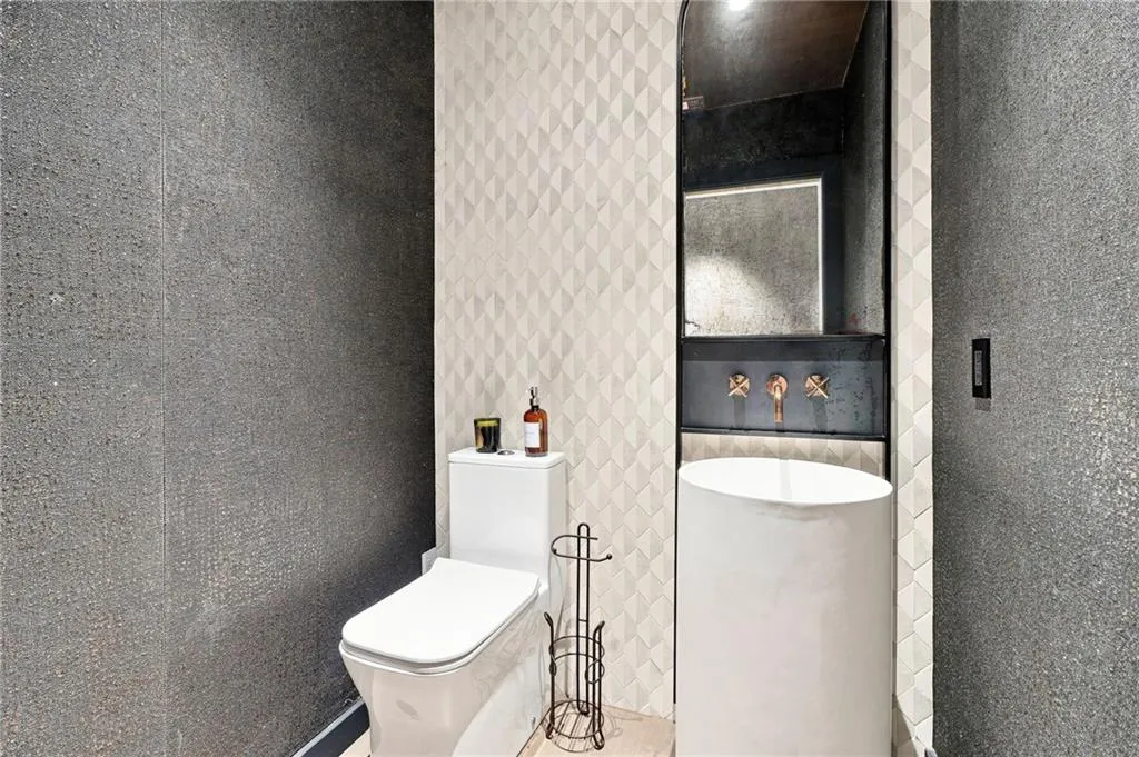 Textured wall coverings, contemporary wall-mounted mirror, integrated vanity lighting, modern freestanding basin, and wall-mounted faucets