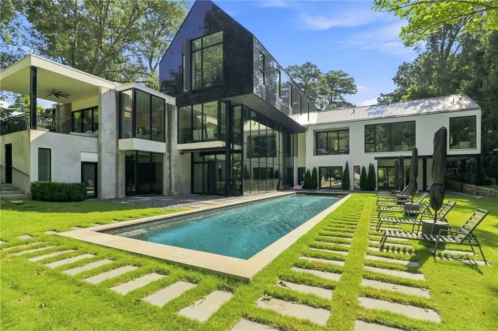 Modern architectural design with a rectangular swimming pool, concrete patio, and an upper-level balcony